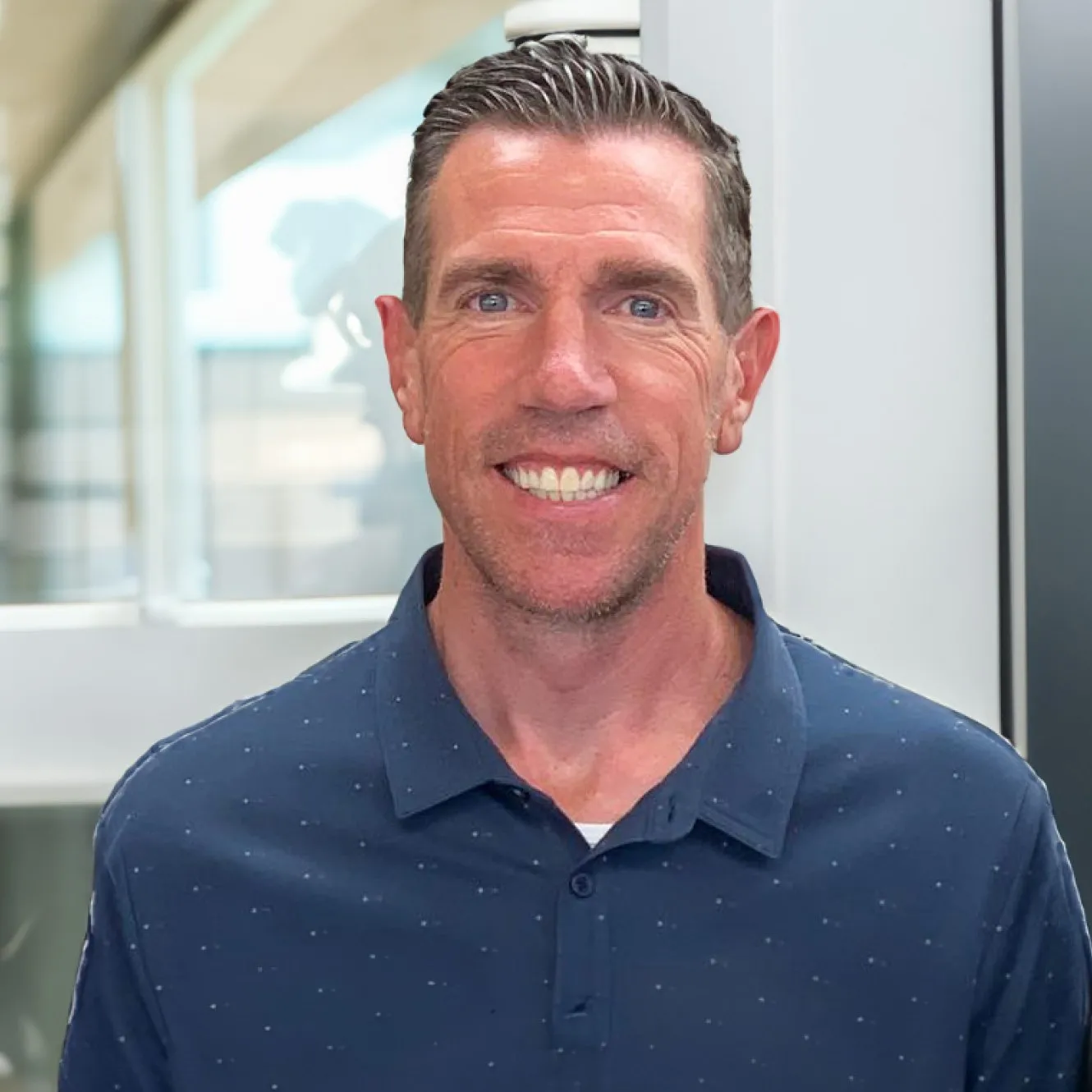 Dr. Jeffrey Potter, orthodontist at Potter Orthodontics, smiling in a professional setting, wearing a navy blue polo shirt, showcasing commitment to creating perfect smiles.